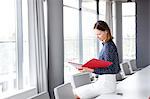 Young businesswoman reading file while sitting on conference table in office