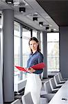 Portrait of confident young businesswoman holding file in conference room