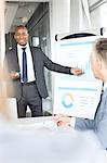 Smiling young businessman giving presentation in board room