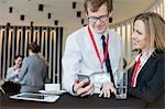 Businesswoman looking at colleague using smart phone during coffee break at convention center