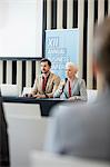 Businesswoman speaking through microphone while sitting with colleague in seminar hall