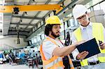 Supervisor with manual worker discussing over clipboard in metal industry