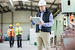 Mature male inspector writing on clipboard while workers in background at factory