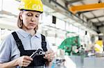 Mature female worker measuring metal with caliper in industry