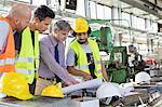 Male supervisor with workers discussing over blueprints in industry