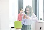 Smiling young businesswoman using mobile phone with male colleague in background at office