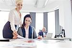 Businesswomen reading book with male colleague in background at office