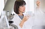 Female college student conducting scientific experiment examining vials in science laboratory classroom