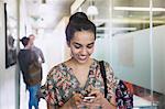 Smiling female college student texting in corridor