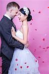 Side view of romantic wedding couple embracing against pink background