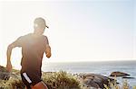 Male triathlete runner running along ocean