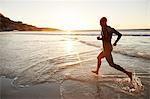 Male triathlete swimmer in wet suit running into ocean surf at sunrise