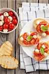 Bruschetta with cherry tomatoes and mozzarella on wooden background, top view