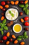 Italian food ingredients – mozzarella, tomatoes, basil and olive oil on black slate background, top view