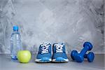 Sport shoes, dumbbells, apple, bottle of water on gray concrete background. Concept healthy lifestyle, sport and diet. Sport equipment.