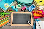 Back to school concept with small chalkboard and multicolor stationery on wooden surface.