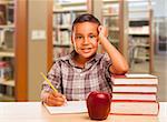 Adorable Hispanic Boy with Books, Apple, Pencil and Paper Studying at the Library.