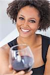 A beautiful happy mixed race African American girl or young woman wearing a black dress and drinking red wine at home