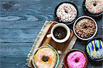 Colorful Donuts breakfast composition with different color styles of doughnuts and fresh coffee on the side over an aged wooden desk background.