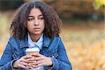 Beautiful mixed race African American girl teenager female young woman outside in autumn or fall looking sad depressed or thoughtful drinking coffee