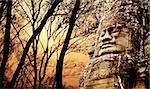 Giant stone face in Prasat Bayon Temple and trees on sunset sky background. Famous landmark Angkor Wat complex, khmer culture, Siem Reap, Cambodia