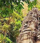 Giant stone face in Prasat Bayon Temple and trees in rainforest. Famous landmark Angkor Wat complex, khmer culture, Siem Reap, Cambodia