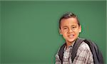 Cute Hispanic Boy with Backpack In Front of Blank Chalk Board.