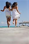 Two young adult girls running along a jetty by the beach.