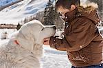 Young boy looking at his dog while playing outside in the snow.