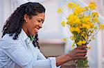 Happy mid adult woman putting a bunch of yellow flowers into a vase outdoors.