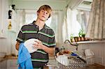 Teenage boy washing dishes in a kitchen.