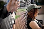 Young man talking to a young woman through a wire link fence.