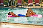 Relaxed mid adult woman floating on an air bed in a swimming pool.