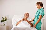 Female nurse laughing with senior male patient lying in hospital bed.