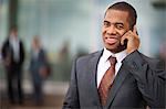 Young businessman smiling thoughtfully into the distance as he talks on his cell phone outside his office building.