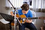 Boy sits playing his guitar.