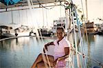 Portrait of mature woman happily relaxed as she is sitting on boat deck in harbour.