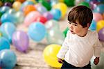 Little boy standing in a room full of balloons.