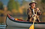 Happy middle aged man canoeing across a lake.
