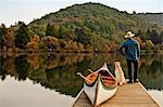 Canoeist standing on the edge of a lake pier with his dog.