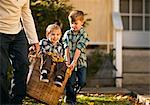 Little boy being carried in the basket full of autumn leaves.