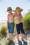Sweden, Gotland, Shirtless boys (6-7, 8-9) in straw hats standing on sand dune at seashore
