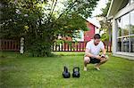 Sweden, Norrland, Vasterbotten, Mature man crouching next to weights on lawn in backyard