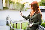 Finland, Pirkanmaa, Tampere, Redhaired woman standing on staircase and using phone