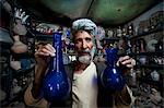 A glass blower holds up blue glass gourd-shaped vases in a trinket shop in Herat, Afghanistan, Asia