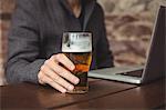 Man holding glass of beer and using laptop at bar