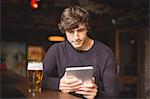 Man with glass of beer using digital tablet in counter at bar