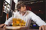 Bartender standing near counter with glasses of beer in bar