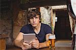 Portrait of man using digital tablet with beer glass on table in bar