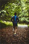 Rear view of athlete running on dirt track in forest